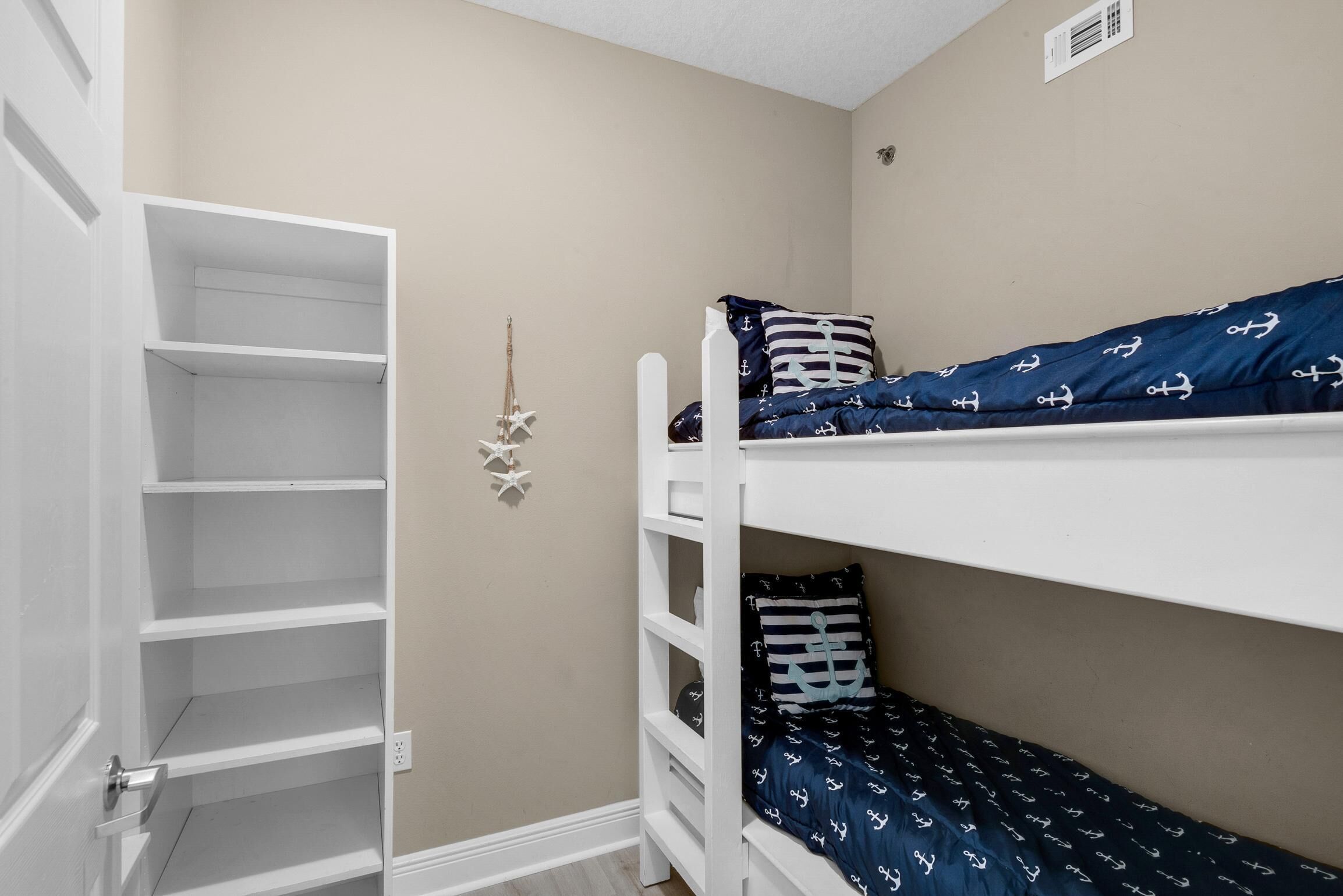 Un lit superposé avec une literie bleu marine et des motifs d’ancres blancs, une étagère blanche et un mur beige orné d’une étoile.