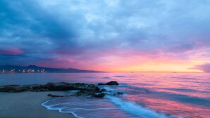 Una playa con costa rocosa y aguas tranquilas que reflejan un cielo al atardecer.