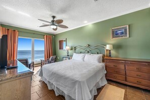 A hotel room with a large bed, a desk with a computer, a ceiling fan, and a view of the ocean. - Riviera Dunes 501 (Pensacola)
