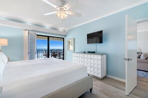 A bedroom with a bed, a ceiling fan, a TV on the wall, a dresser, and a door leading to a balcony with a view. - Shipwatch D604 (Pensacola)