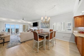 A spacious living room with a dining area, a kitchen, and a balcony with white shutters. - Shipwatch D604 (Pensacola)