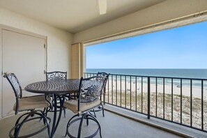 A balcony with a table and chairs, a view of the beach, and a door. - Shipwatch D604 (Pensacola)