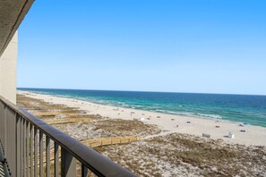 Vista de una playa desde un balcón con barandilla de madera, playa de arena y océano.