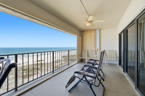 A balcony with a view of the beach, a ceiling fan, and a few chairs.