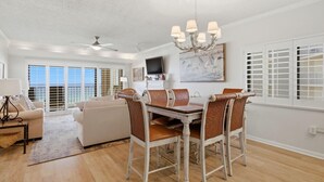 A spacious living room with a dining area, large windows, and a ceiling fan. - Shipwatch D604 (Pensacola)