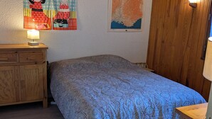 Ein Schlafzimmer mit einem gemusterten Bettüberwurf, Holzmöbeln und Wanddekorationen, darunter eine Karte und Zeichentrickfiguren.