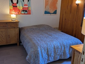 A bedroom with a patterned bedspread, wooden furniture, and wall decorations including a map and cartoon characters.