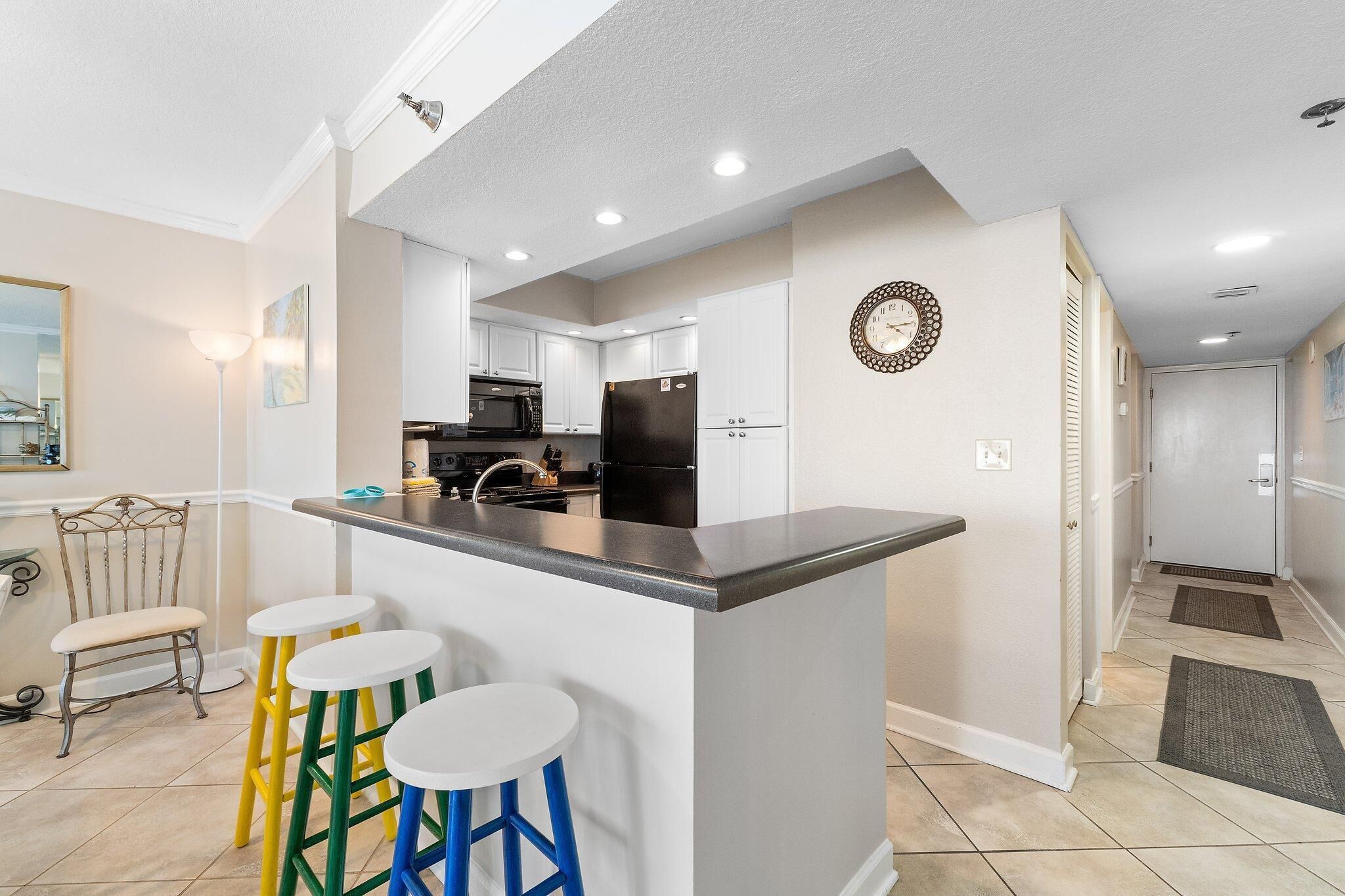 A modern kitchen with white cabinets, a black refrigerator, and a central island with stools.