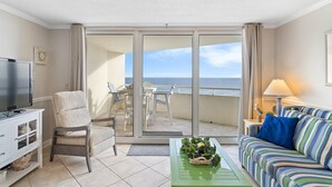 A living room with a TV, a sofa, a chair, a table with a plant, and a balcony with a view of the sea. - Perdido Sun 512 (Pensacola)