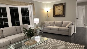 A living room with a beige sofa, a glass coffee table, a patterned rug, a wall-mounted lamp, and a framed certificate. - Quiet & cozy home, bring the whole family. (Monroe Township)