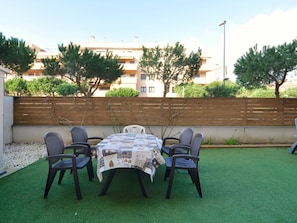 Une terrasse extérieure avec une table ronde et six chaises, entourée de gazon synthétique.