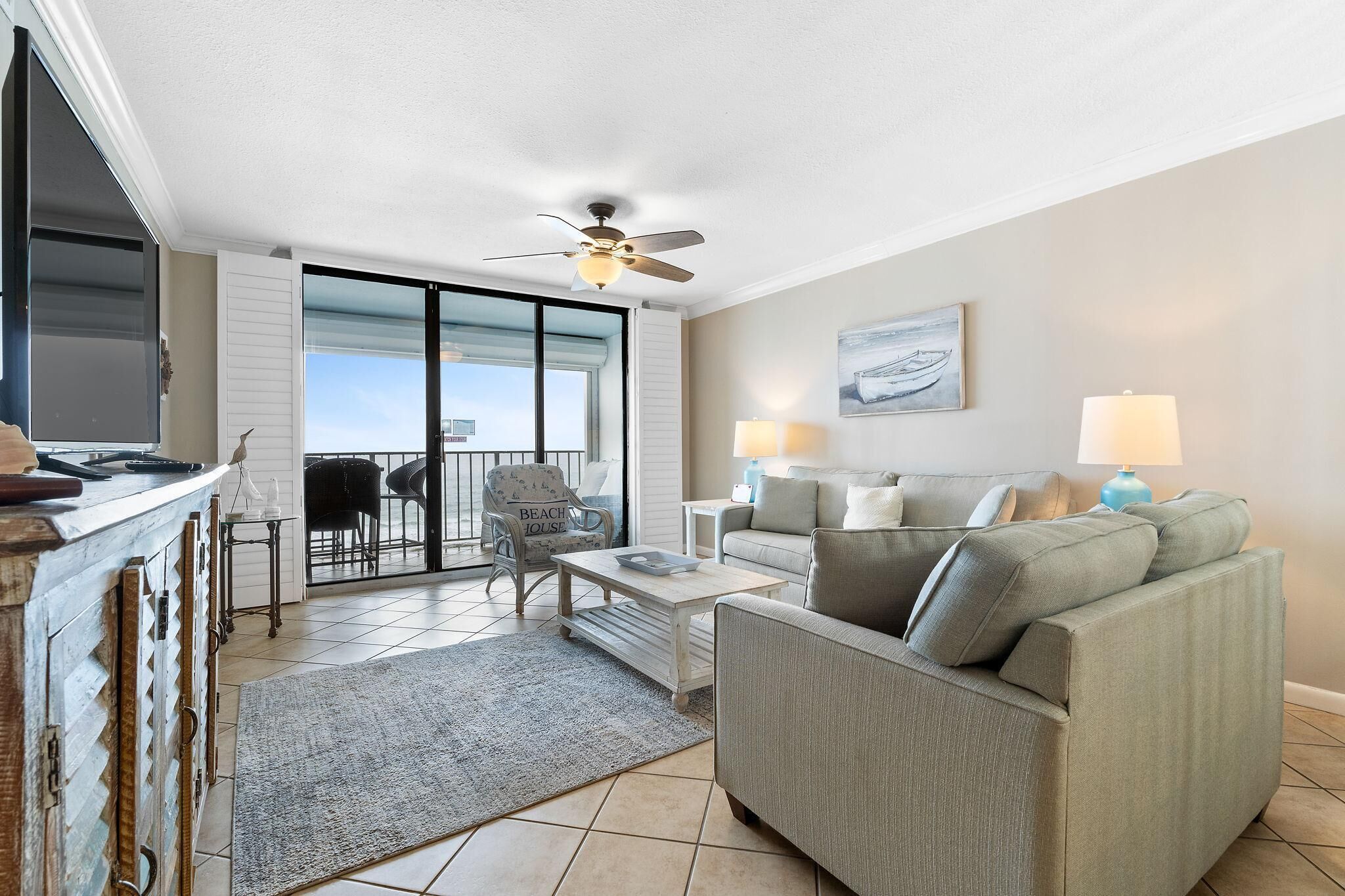 A living room with a sofa, a coffee table, a ceiling fan, and a view through a sliding glass door to the outside.