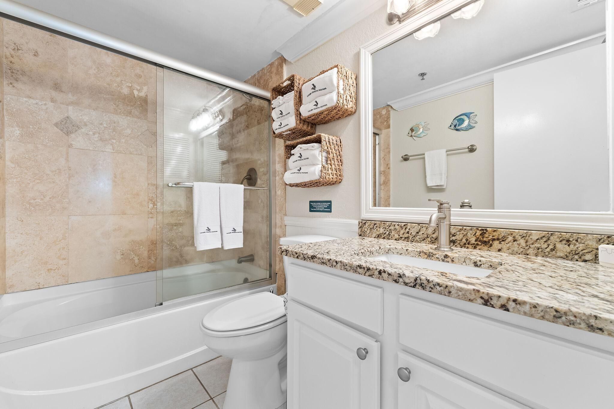 A modern bathroom with a glass shower enclosure, a white toilet, a granite countertop, and a large mirror.