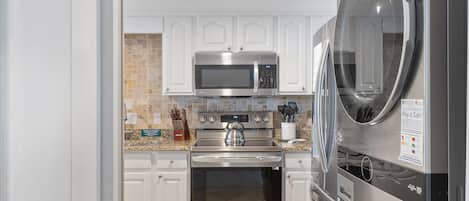 A modern kitchen with white cabinets, a stainless steel microwave, oven, and refrigerator.