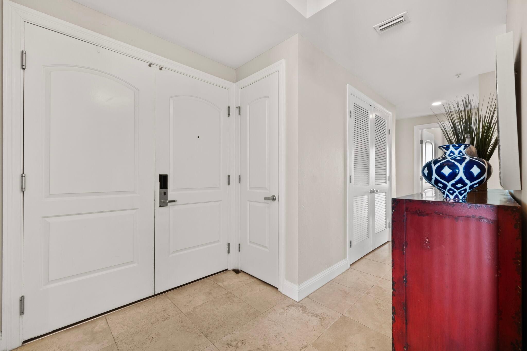 A hallway with white double doors, a red podium, and a decorative vase.