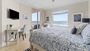 Un dormitorio con cama, escritorio, silla, televisión y vista al océano.