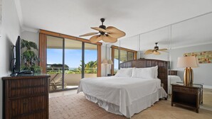 A bedroom with a large bed, two ceiling fans, a wooden nightstand, a TV on a cabinet, and a view of the outdoors. - Eden East 101 (Pensacola)