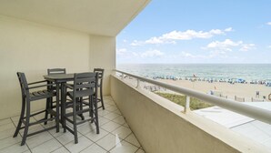 Balcón con mesa y sillas que da a una playa con gente y sombrillas.