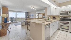 Una cocina moderna con una isla central, microondas empotrado y horno. Cuenta con un comedor con sillas y una mesa, además de un ventanal con vistas.