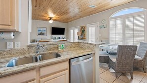 A kitchen with a wooden ceiling, a built-in dishwasher, a sink, and a dining area with wicker chairs.
