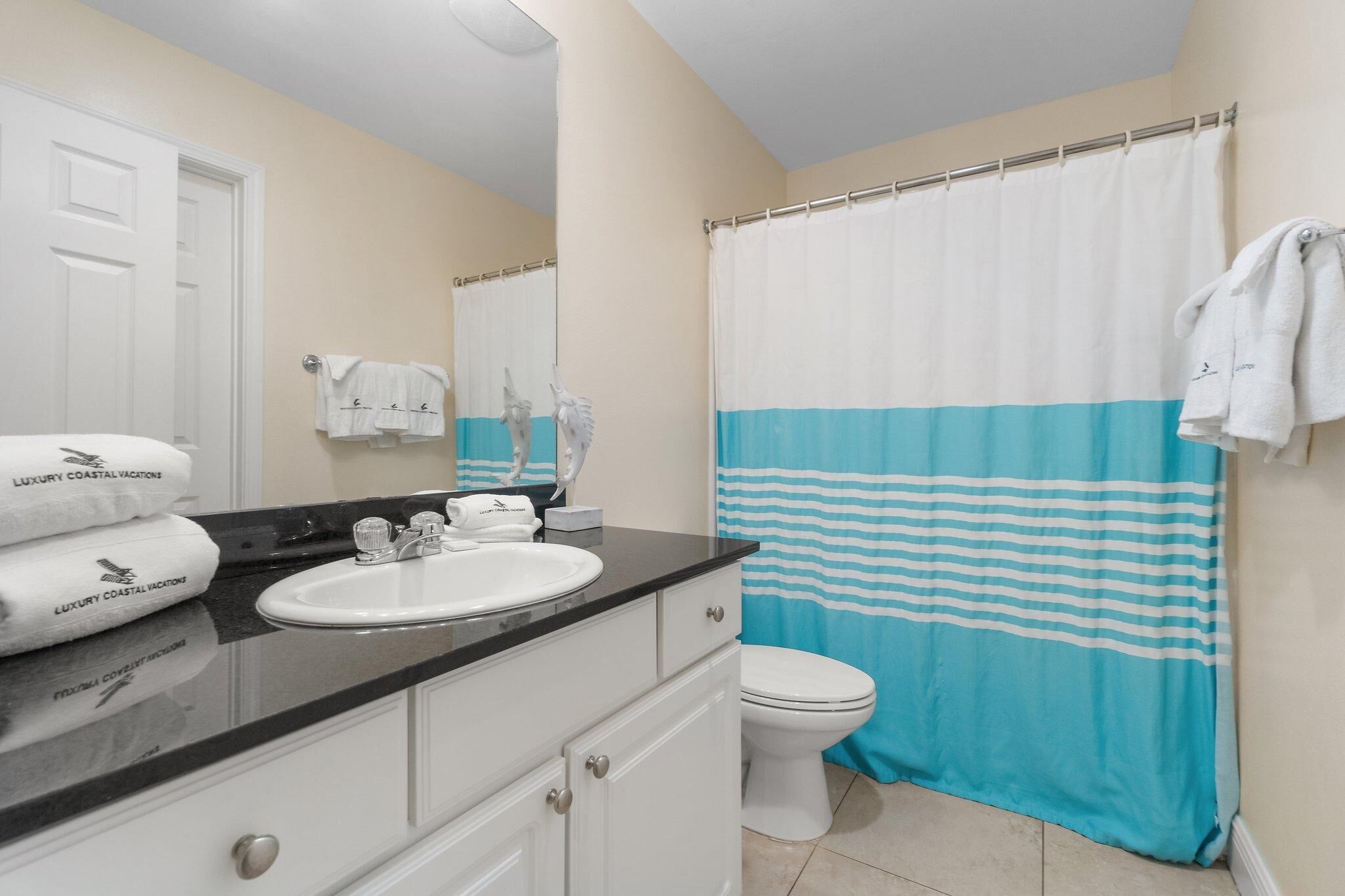 A bathroom with a white sink, a toilet, and a shower curtain with blue stripes. There are towels on the sink and a towel rack on the wall.