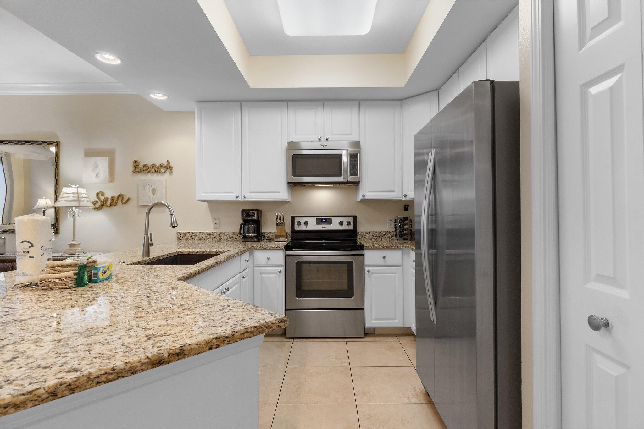 A modern kitchen with white cabinets, a granite countertop, a stainless steel refrigerator, and a built-in microwave.