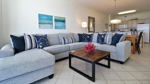 Ein modernes Wohnzimmer mit einem grauen Ecksofa, einem Holztisch und einer Küche im Hintergrund.