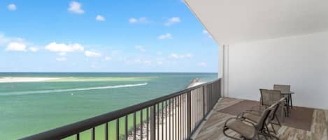A balcony with a view of the ocean, equipped with wicker chairs and a table.