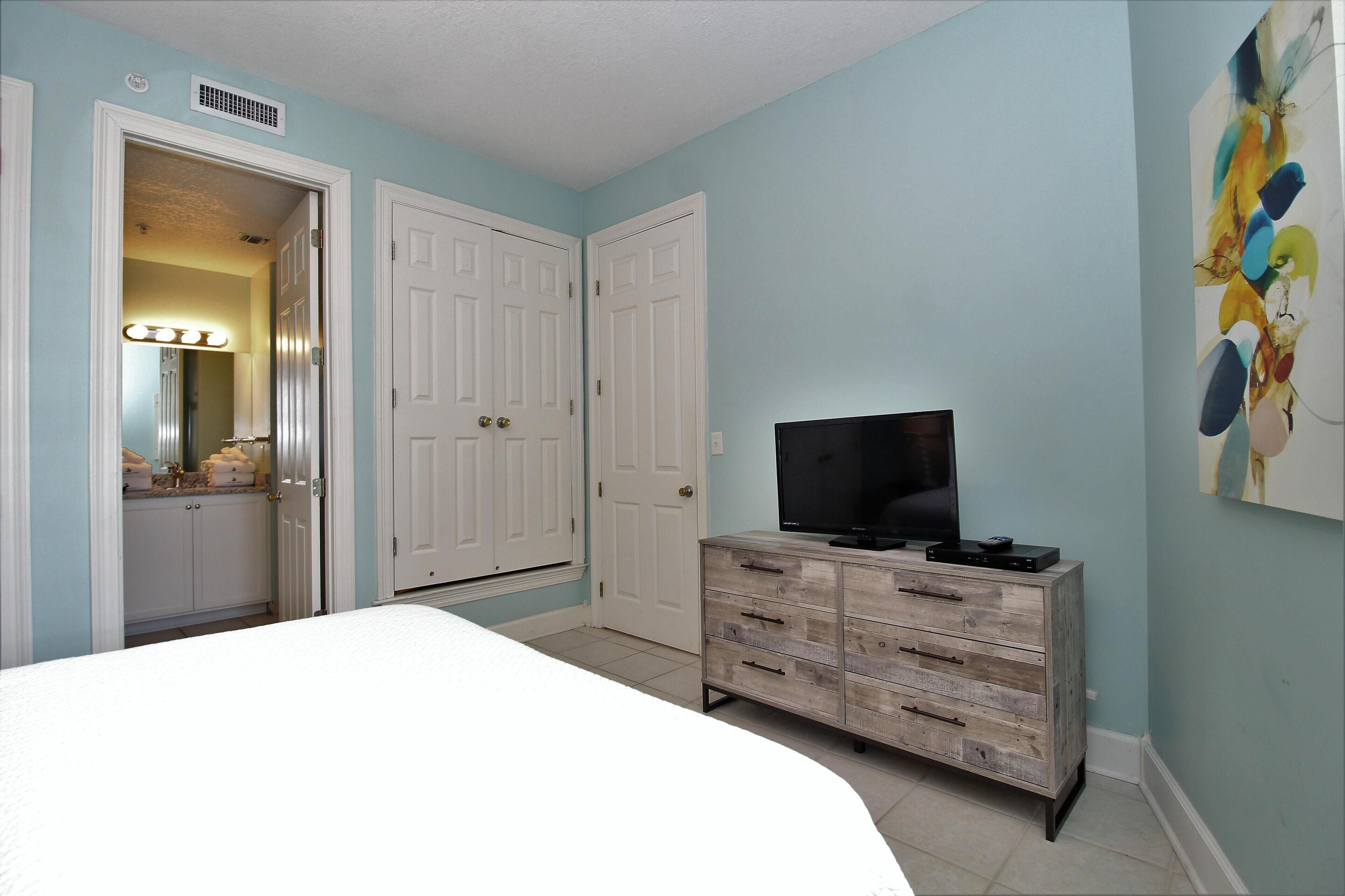 A bedroom with a bed, a dresser, a television, and two doors.