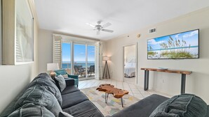 A living room with a large gray sofa, a wooden coffee table, and a television on the wall. - Enclave 506 (Orange Beach)