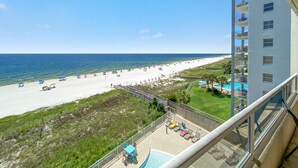 A view of a beach from a balcony with a pool and lounge chairs. - Enclave 506 (Orange Beach)