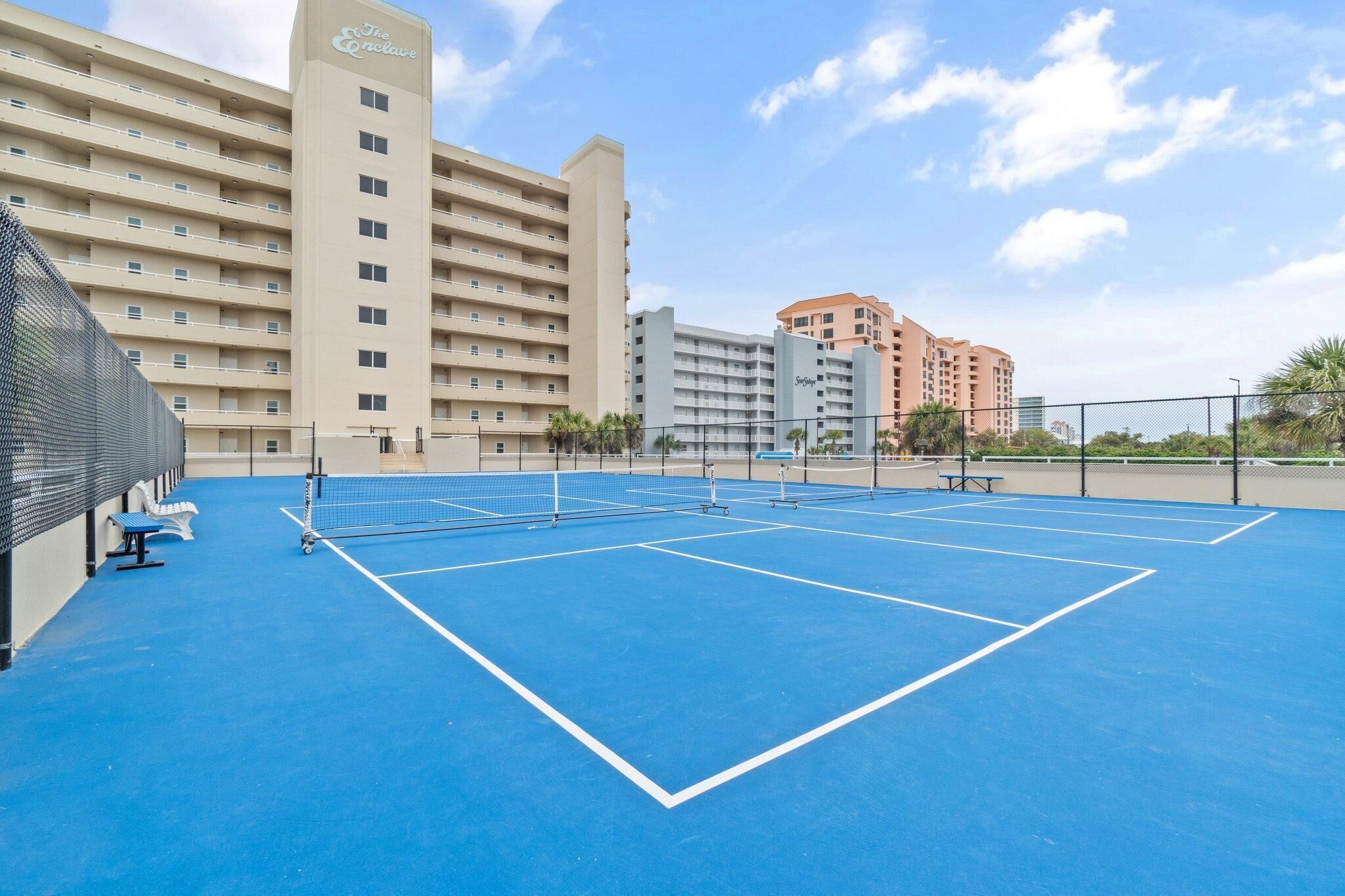 A tennis court with a net, benches, and a fence.
