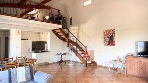 A spacious living area with a high ceiling, wooden beams, a staircase, a dining area, and a kitchen. - Double Family Villa,12 people with Pool near Cannes (Fréjus)