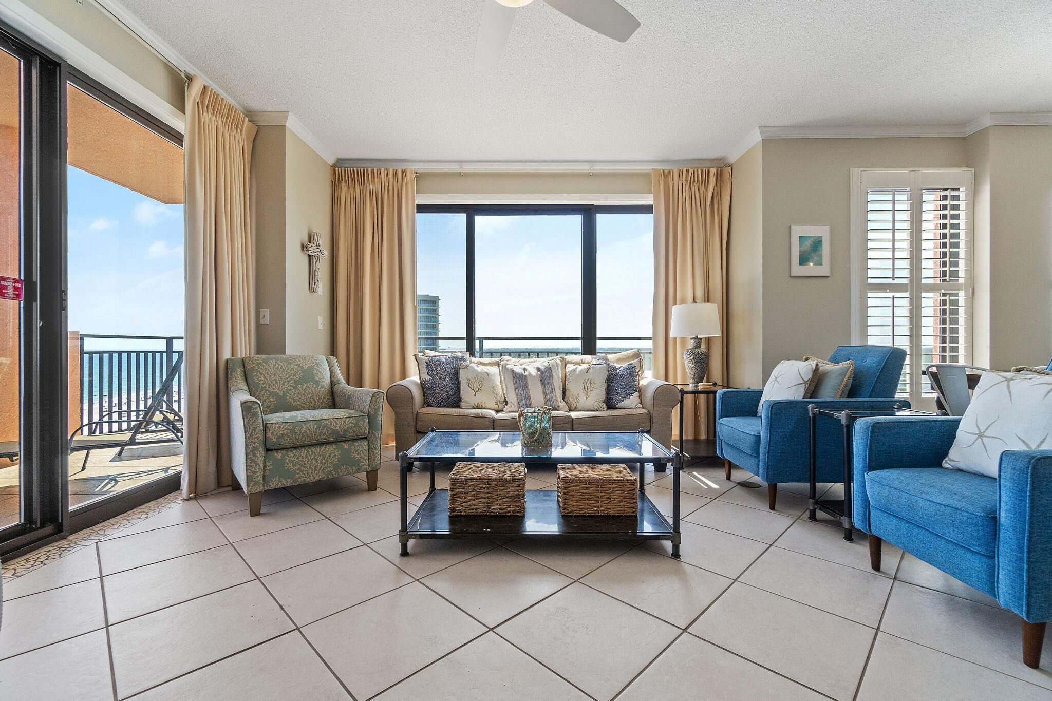 A spacious living room with a glass coffee table, two sofas, a chair, and a balcony with curtains.