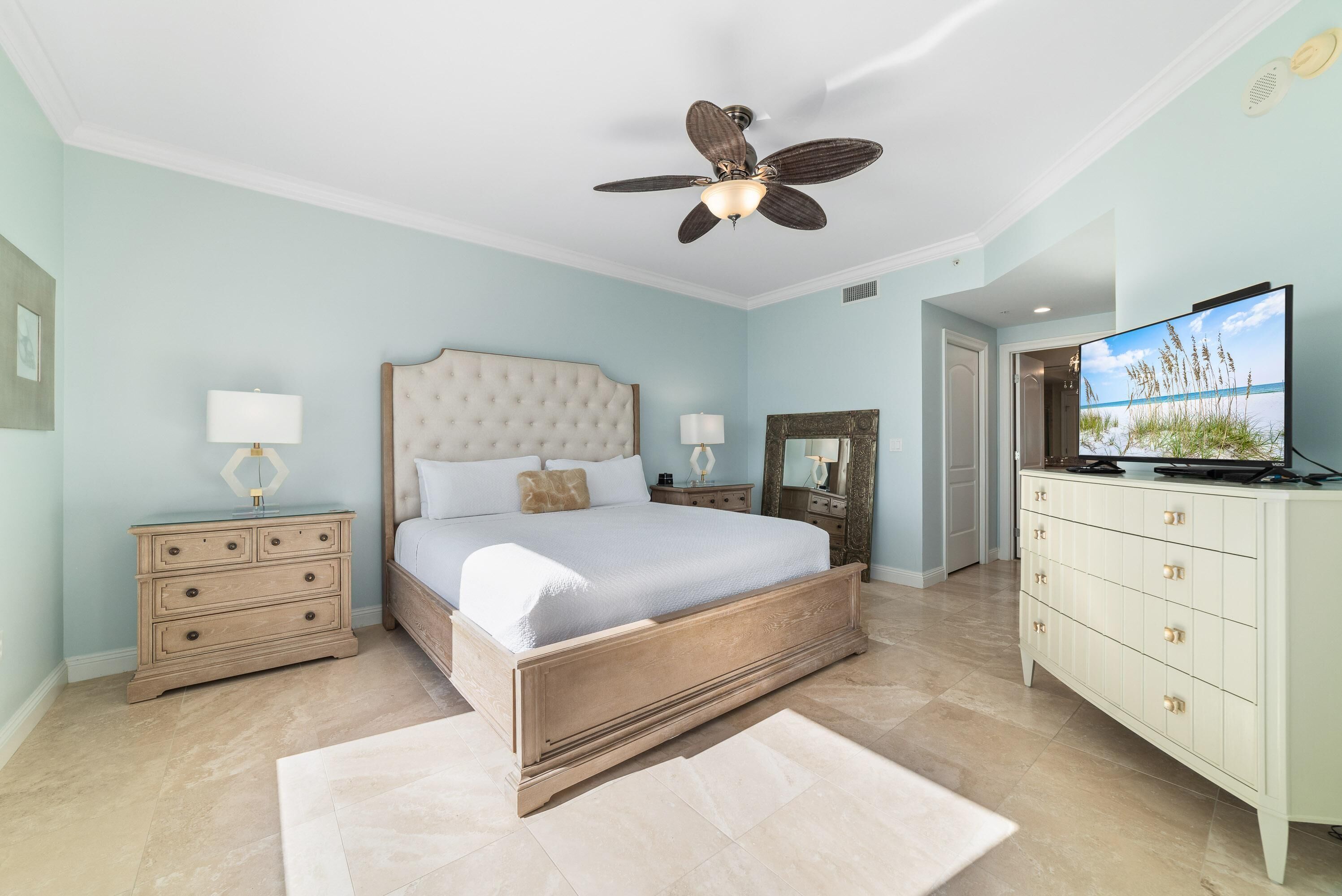 A bedroom with a large bed, a ceiling fan, a dresser, and a television.