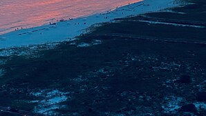 A coastal landscape with a sunset over the ocean, a beach with people, and a pier in the distance. - Phoenix VII 1401 (Orange Beach)