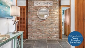 A hallway with a brick wall, a sign reading "BEACH HOUSE ORANGE BEACH, AL", a round mirror, and a lamp with a starfish base. - Phoenix VII 1401 (Orange Beach)