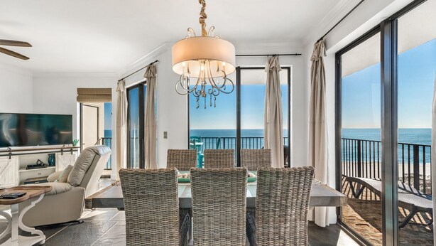 A spacious balcony with a view of the sea, a dining area with wicker chairs, a large chandelier, and a flat-screen TV. - Phoenix VII 1401 (Orange Beach)