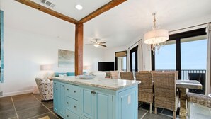 A kitchen with blue cabinets, a marble island, wicker furniture, and a chandelier. - Phoenix VII 1401 (Orange Beach)