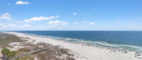 Ein Strand mit einer langen Mole, sandigem Ufer und blauem Himmel.