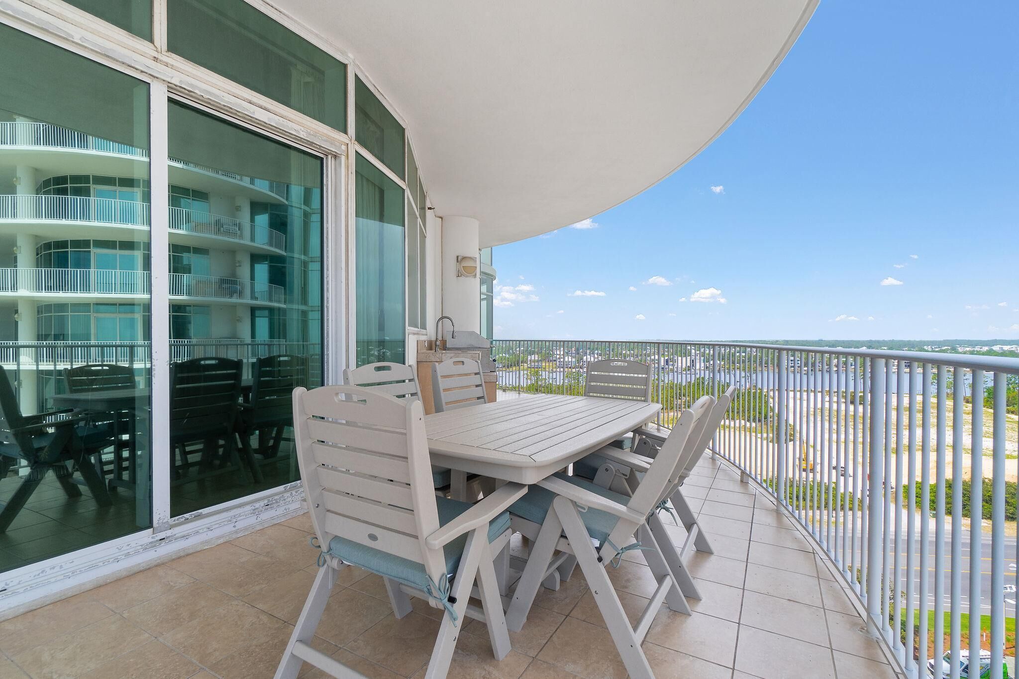 Een balkon met een witte tafel en stoelen, een glazen deur naar een meerlaags interieur en uitzicht op de zee.
