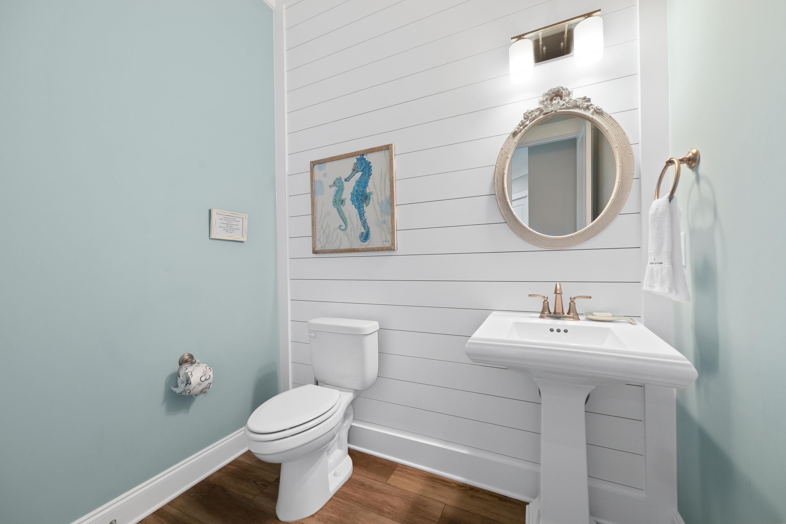 Een badkamer met een wit toilet, een wastafel op een zuil, een spiegel en een afbeelding van een zeepaardje in een lijst aan de muur.