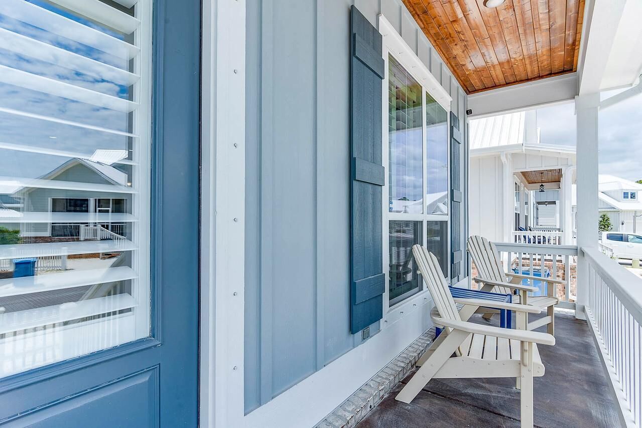 A covered porch with white railings and two Adirondack chairs.