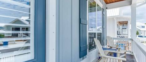 A covered porch with white railings and two Adirondack chairs.