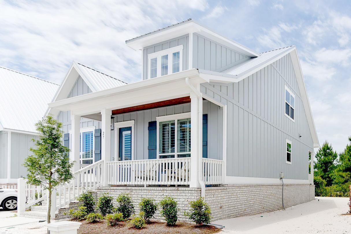 A two-story house with a front porch, a garage, and a small front yard with shrubs.