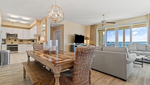 A spacious living area with a wooden dining table, wicker chairs, a grey sofa, and a TV. - Beach Colony Tower Penthouse 17C (Pensacola)