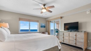 A bedroom with a large bed, a ceiling fan, a TV, and a view of the ocean. - Sandy Key 713 (Pensacola)