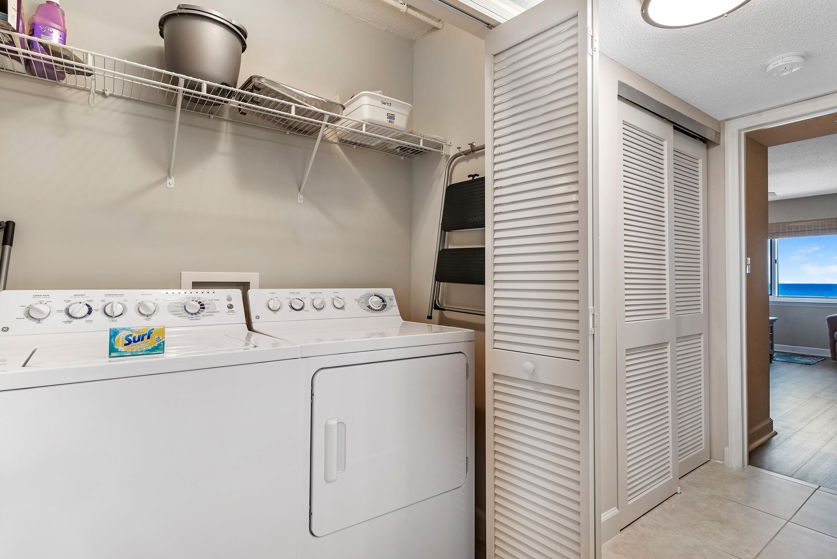 A laundry area with a washer and dryer, a shelf with storage containers, and a sliding closet door.