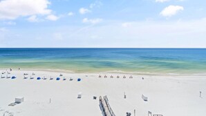 A beach with white sand, clear blue water, and a few umbrellas and lounge chairs. - Perdido Skye 65 (Pensacola)