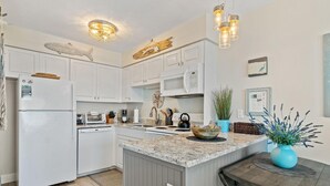 A modern kitchen with white cabinets, a granite countertop, and a central island with a blue vase. - Perdido Skye 65 (Pensacola)